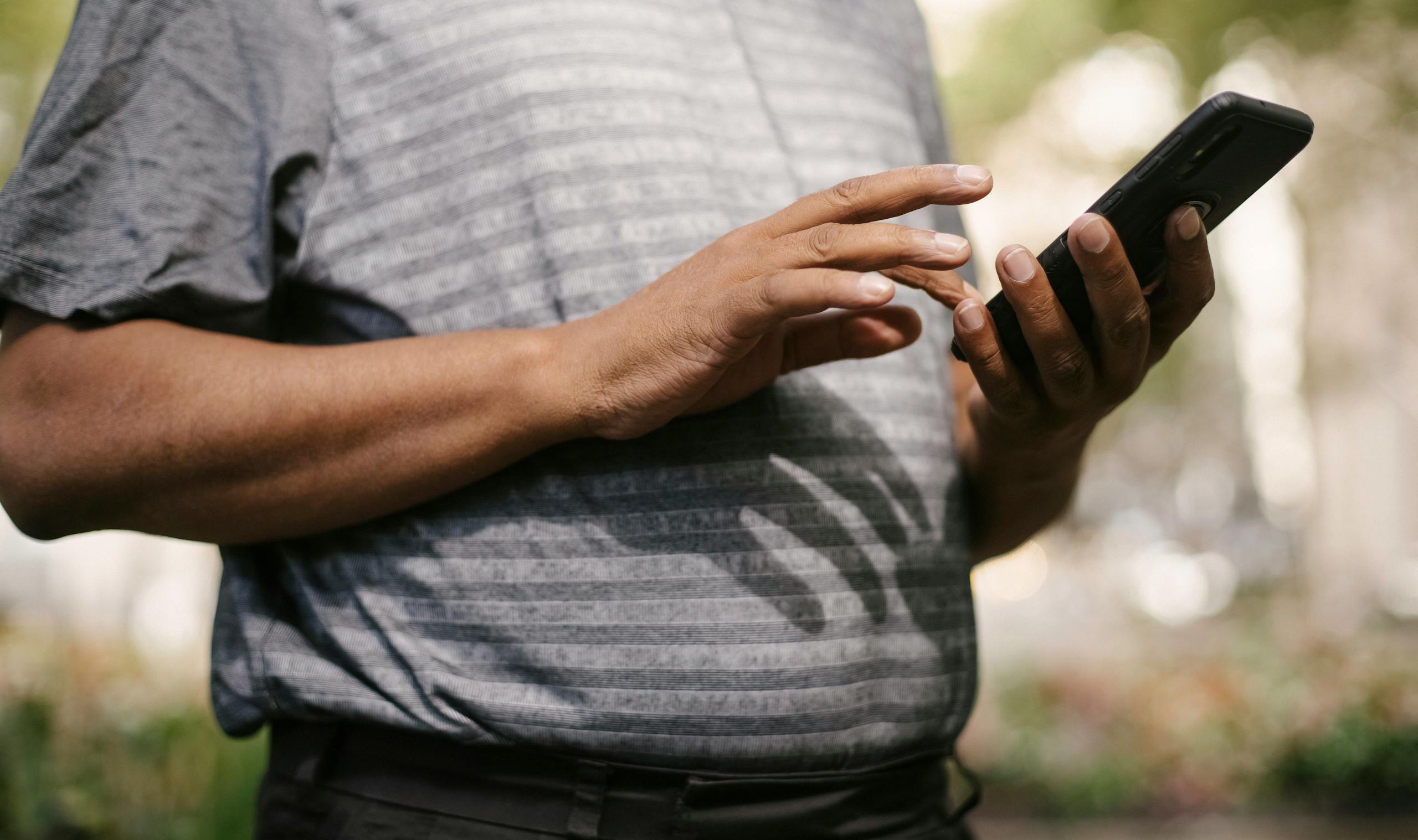 Crop anonymous male in casual clothes using smartphone on blurred background of street